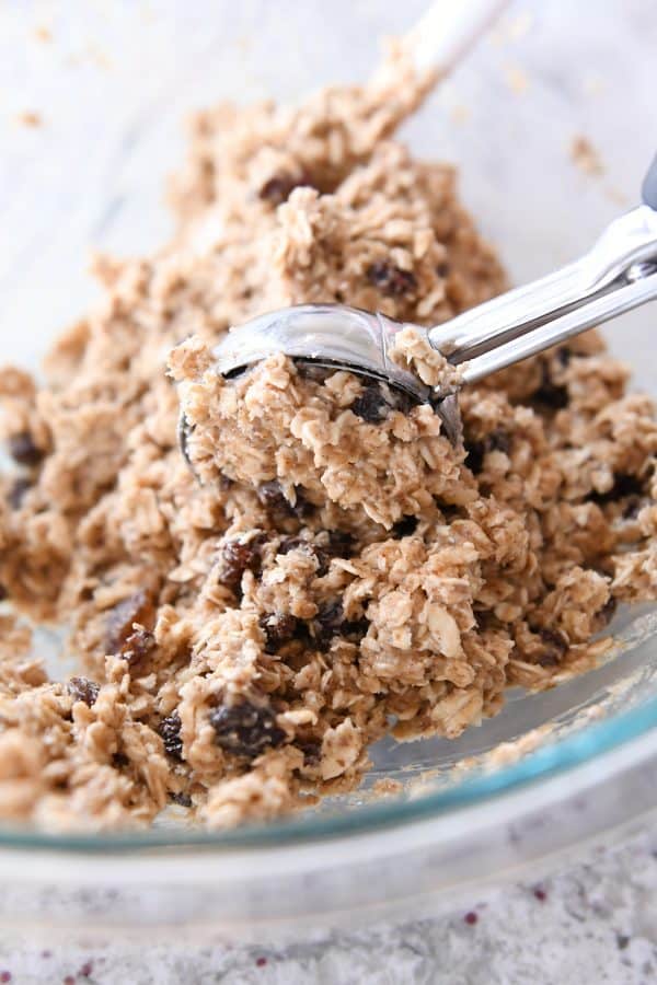 An ice cream scoop scooping out oatmeal cookie dough from a glass bowl.