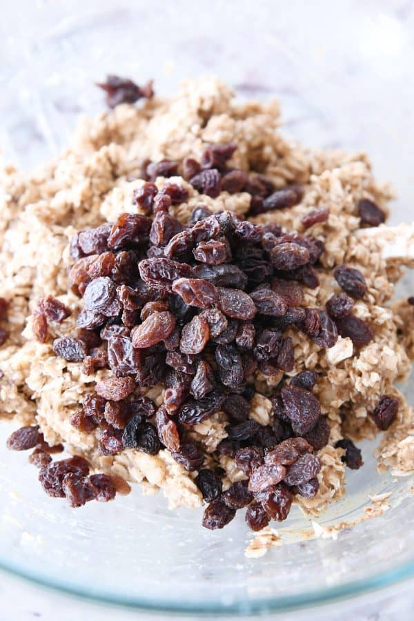 Adding raisins to breakfast cookie dough in a glass bowl.