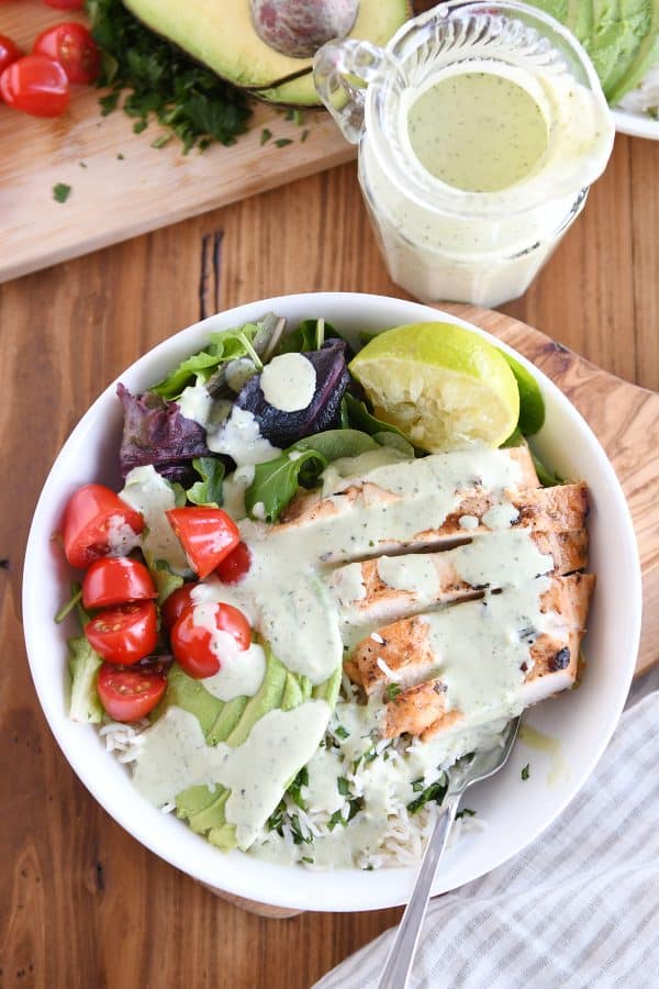 Top down view of honey chipotle lime chicken bowls in white bowl with tomatoes, avocado lime dressing, and tomatoes.