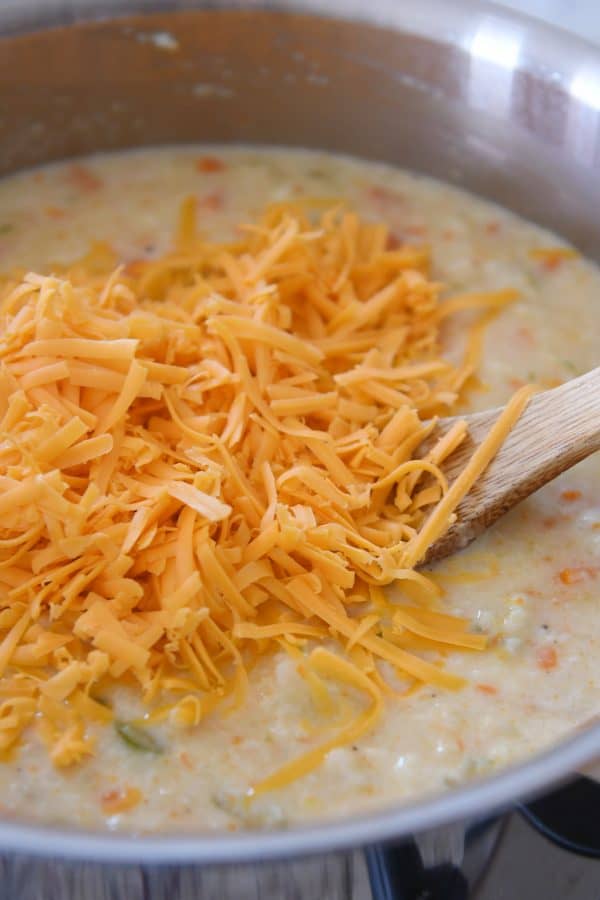 Adding shredded cheddar cheese to cauliflower soup.