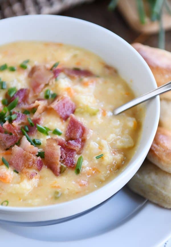 Bowl of loaded cheesy cauliflower soup with rolls.