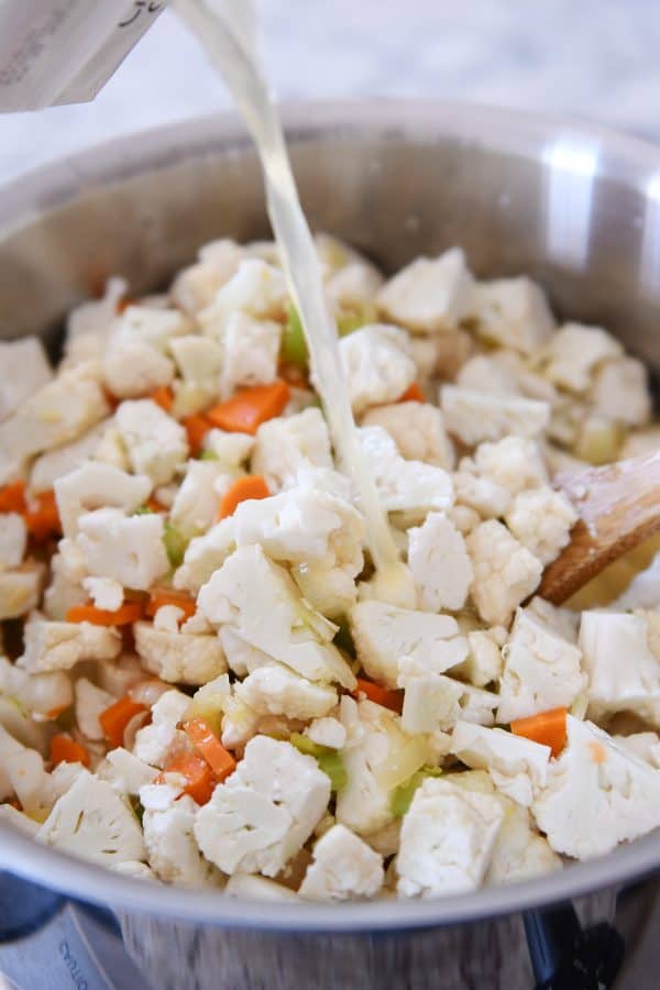 adding broth to cauliflower, carrots, and celery for cheesy cauliflower soup