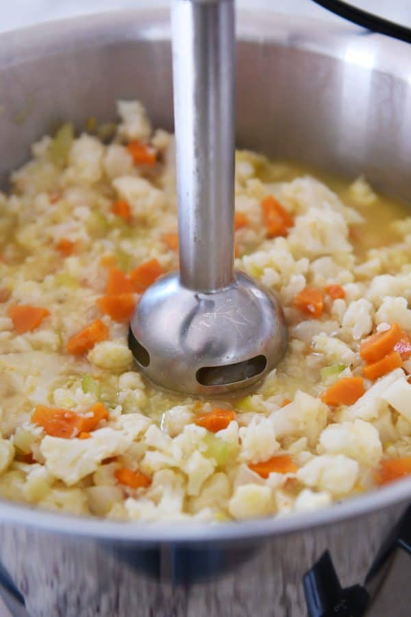 Blending cauliflower, carrots, and celery with immersion blender.