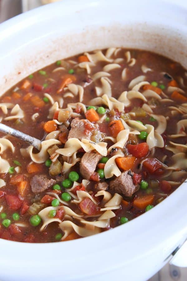 White slow cooker filled with beef vegetable noodle soup.
