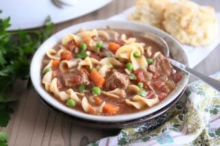 slow cooker beef vegetable noodle soup with spoon in gray ceramic bowl