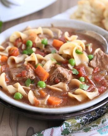 slow cooker beef vegetable noodle soup with spoon in gray ceramic bowl