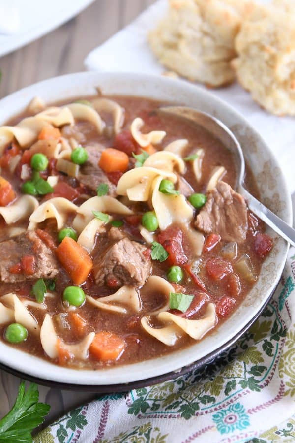 Slow cooker beef vegetable noodle soup with spoon in gray ceramic bowl.