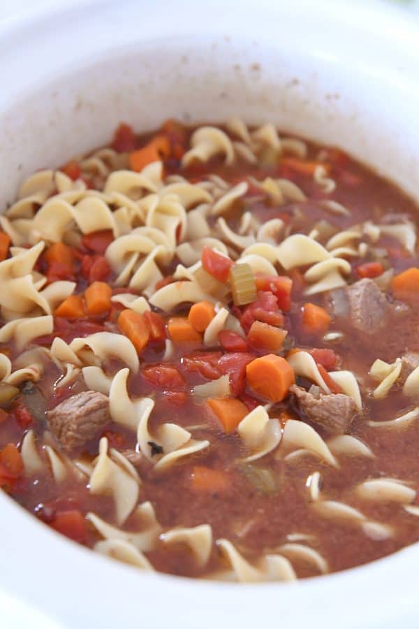 white slow cooker filled with beef vegetable noodle soup