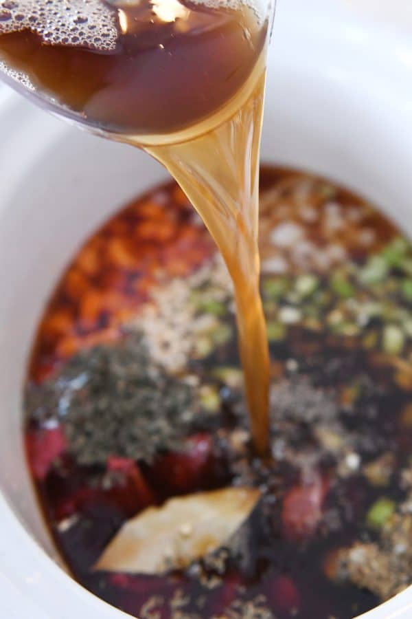 Adding beef broth to slow cooker for beef vegetable noodle soup.