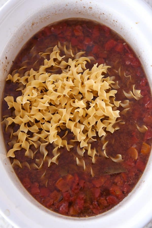 Adding dry egg noodles to slow cooker for beef noodle soup.