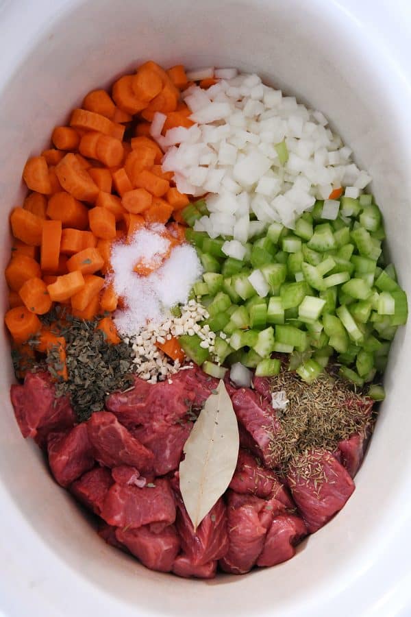 Top down view of beef, veggies, and seasonings in slow cooker.