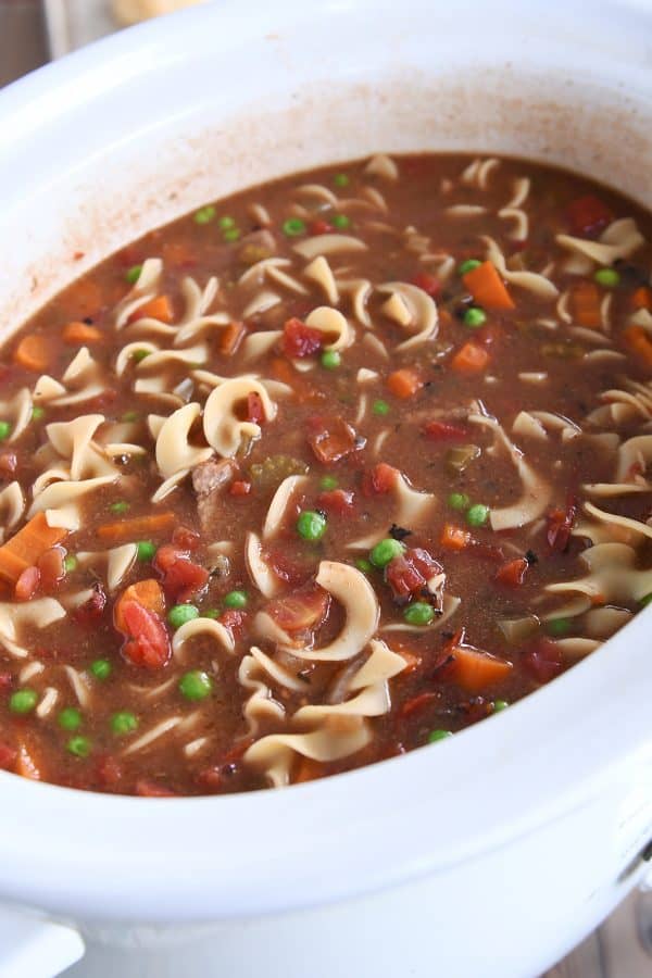 White slow cooker filled with beef vegetable noodle soup.