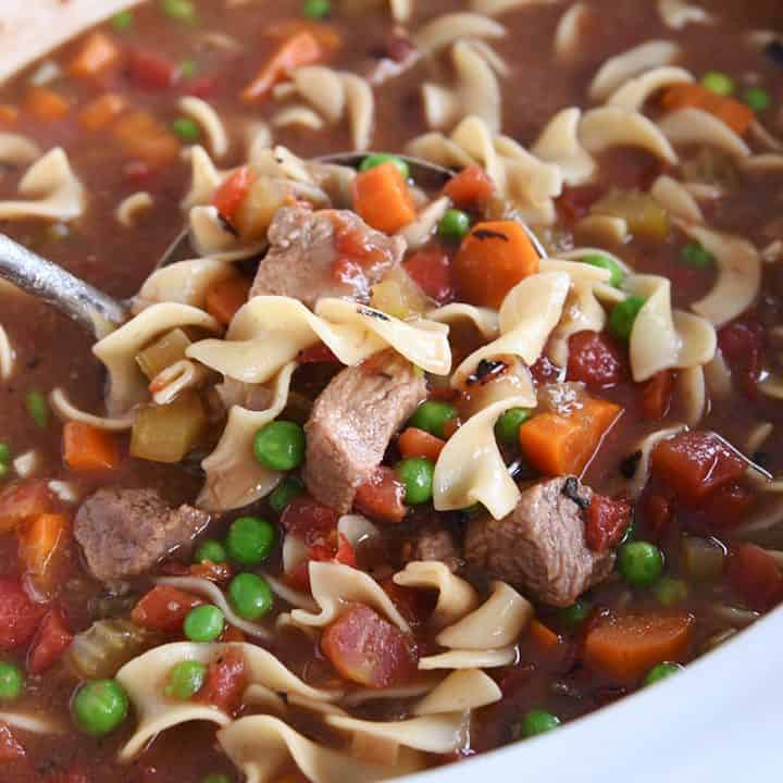 white slow cooker filled with beef vegetable noodle soup