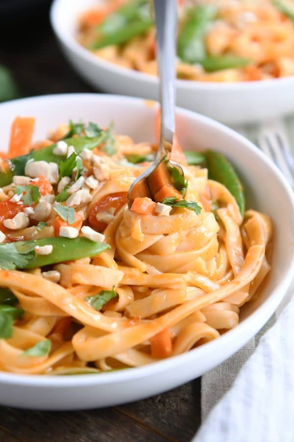 Twirling instant pot red coconut curry noodles with fork in white bowl.