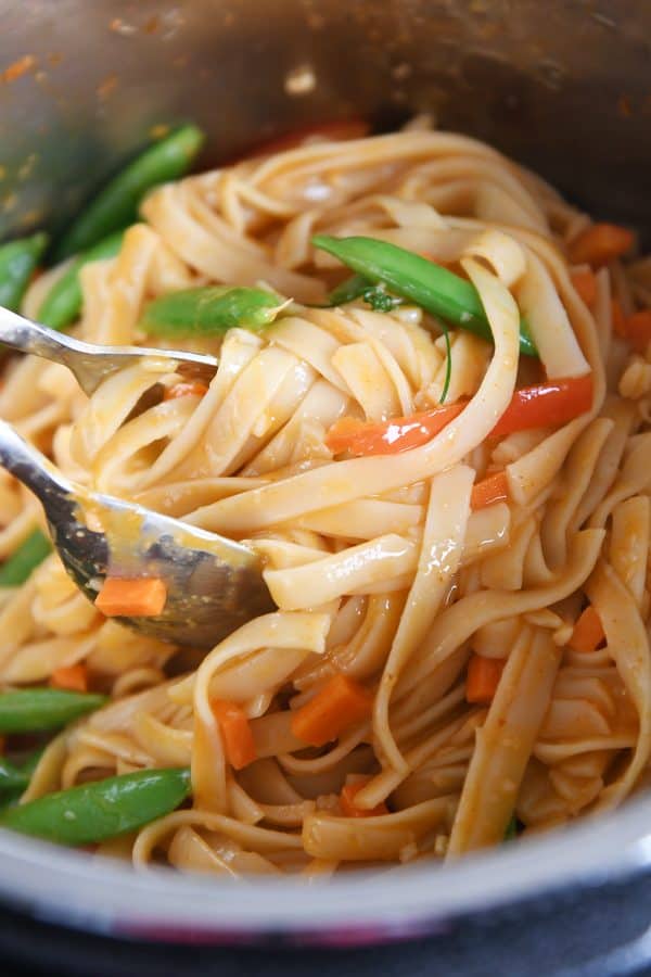 Stirring noodles and veggies together in instant pot for red coconut curry noodles.