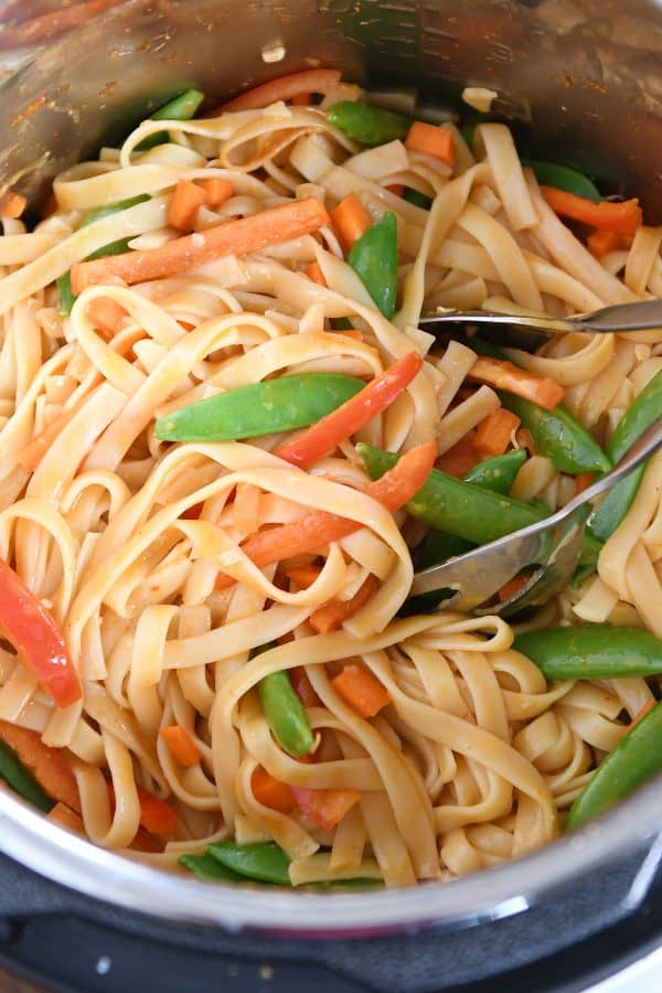 Stirring noodles and veggies together in instant pot for red coconut curry noodles.