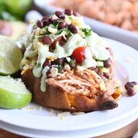Loaded stuffed bbq chicken sweet potato with cilantro lime dressing on white plate