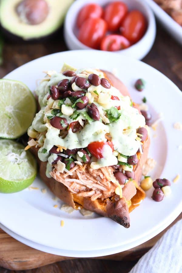 A stuffed sweet potato on a white plate with two limes next to it.