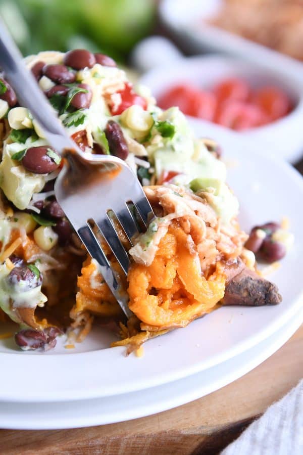 Using fork to to take a bite out of Loaded stuffed bbq chicken sweet potato with cilantro lime dressing on white plate