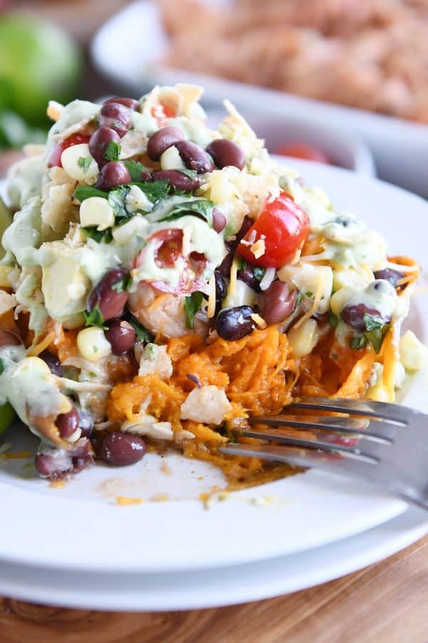 Cutting into loaded stuffed bbq chicken sweet potato with cilantro lime dressing on white plate 