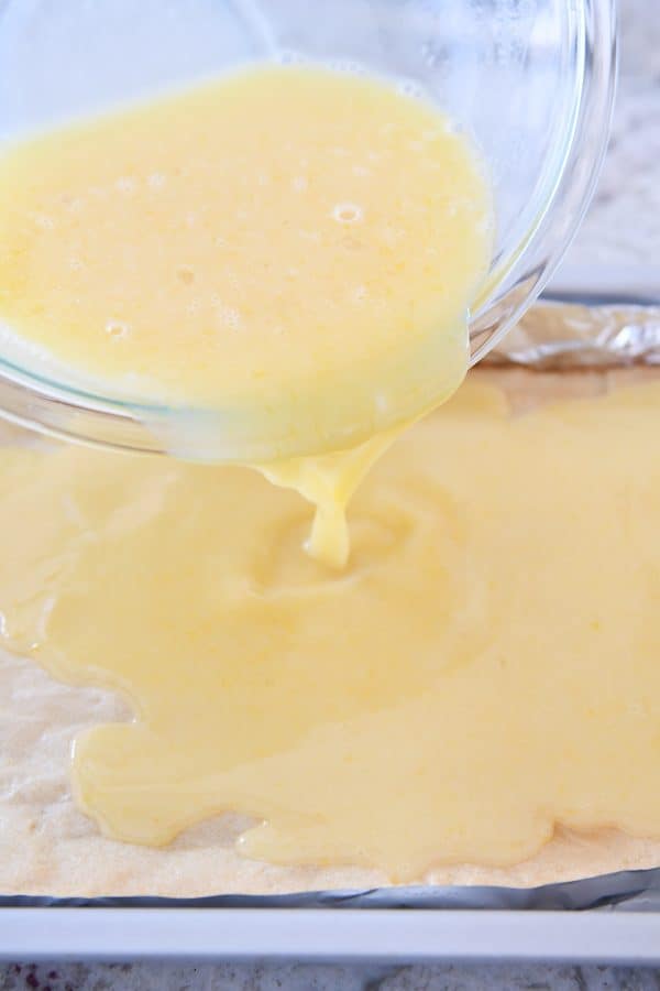 Pouring lemon filling over baked white chocolate brownies.