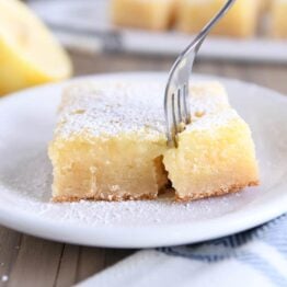 fork pulling corner piece off of lemon bar white chocolate brownie on white plate