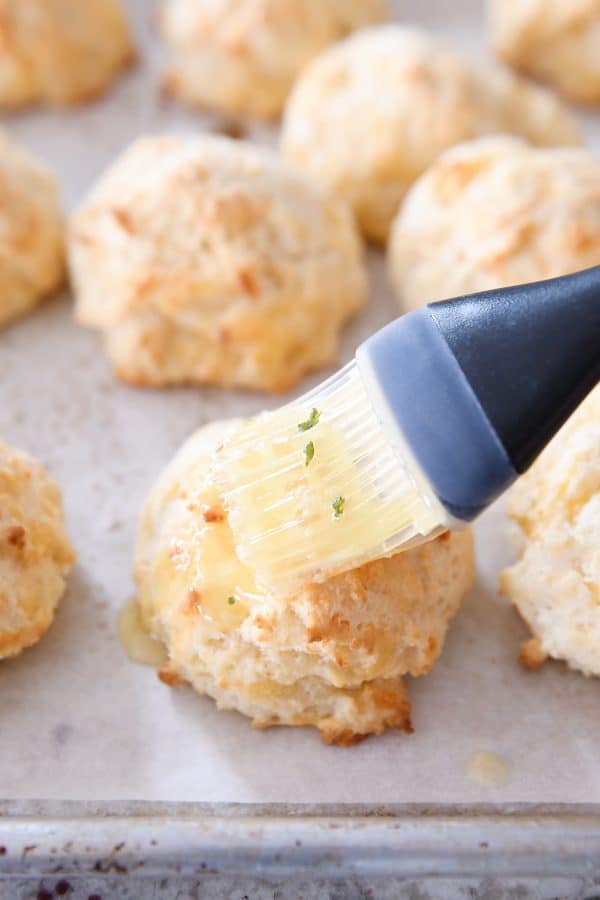 Brushing hot baked cheesy garlic drop biscuit with butter.