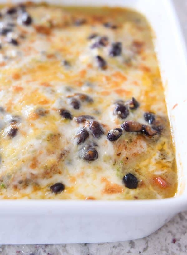 Close up of corner of cheesy chicken enchilada bake in white ceramic pan.