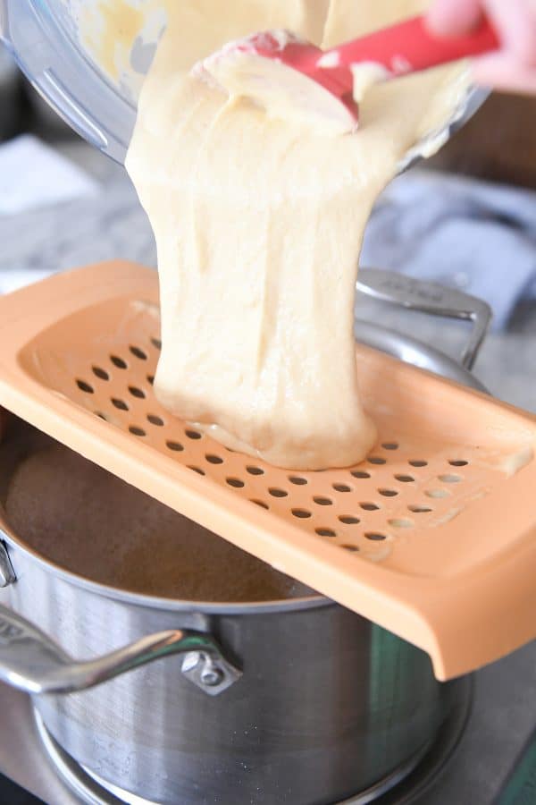 pouring spaetzle batter onto spaetzle maker over pan of hot broth