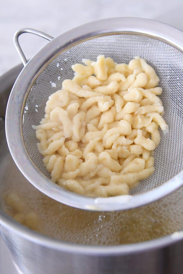Lifting out cooked spaetzle with strainer.