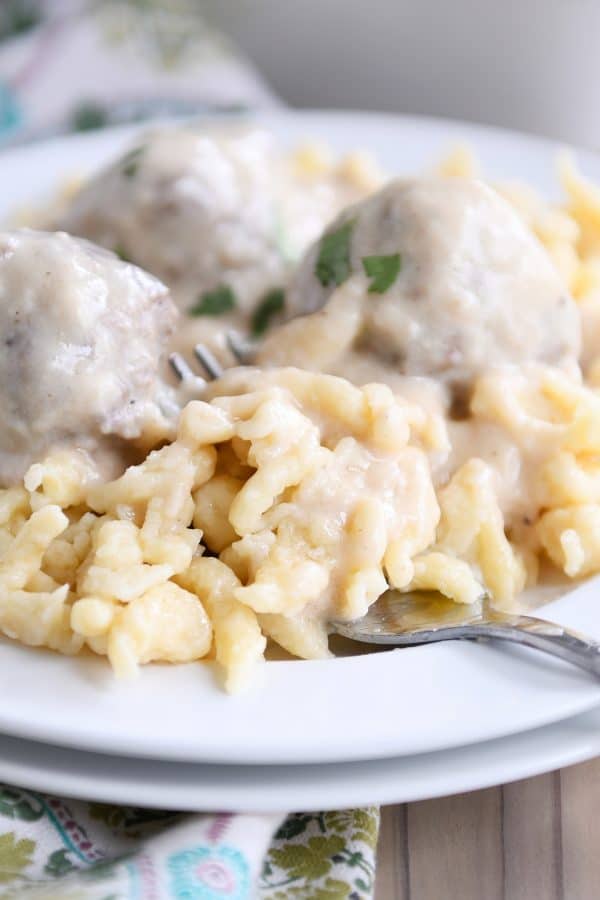 White plate with homemade German spaetzle noodles and meatballs and fork.