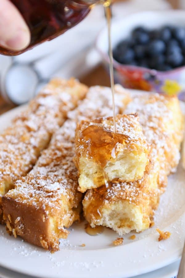 Crunchy baked french toast sticks with syrup getting poured on top.