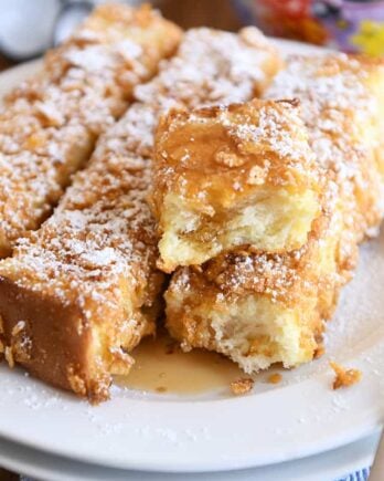crunchy baked french toast sticks on white plate with powdered sugar and syrup