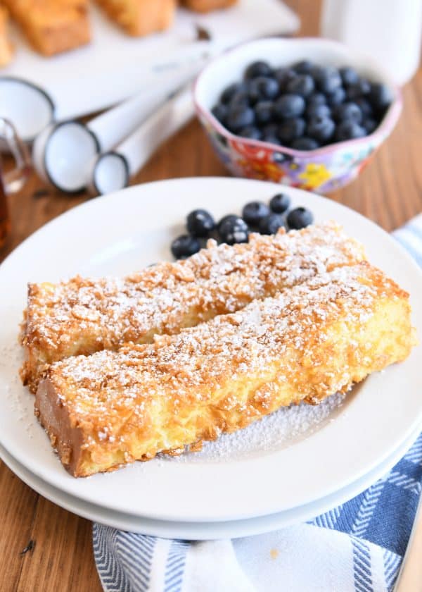 Two crunchy baked french toast sticks on white plate with powdered sugar and blueberries.