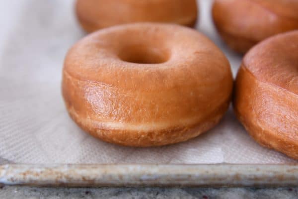 Homemade glazed donuts on paper towel lined baking sheet.