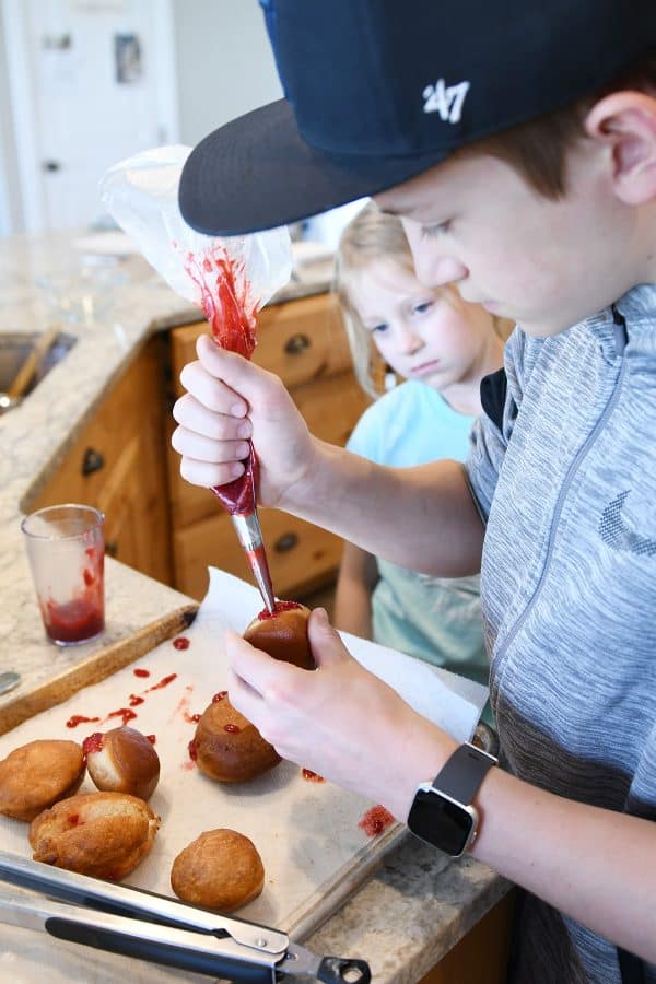 Piping raspberry jam into homemade donuts.