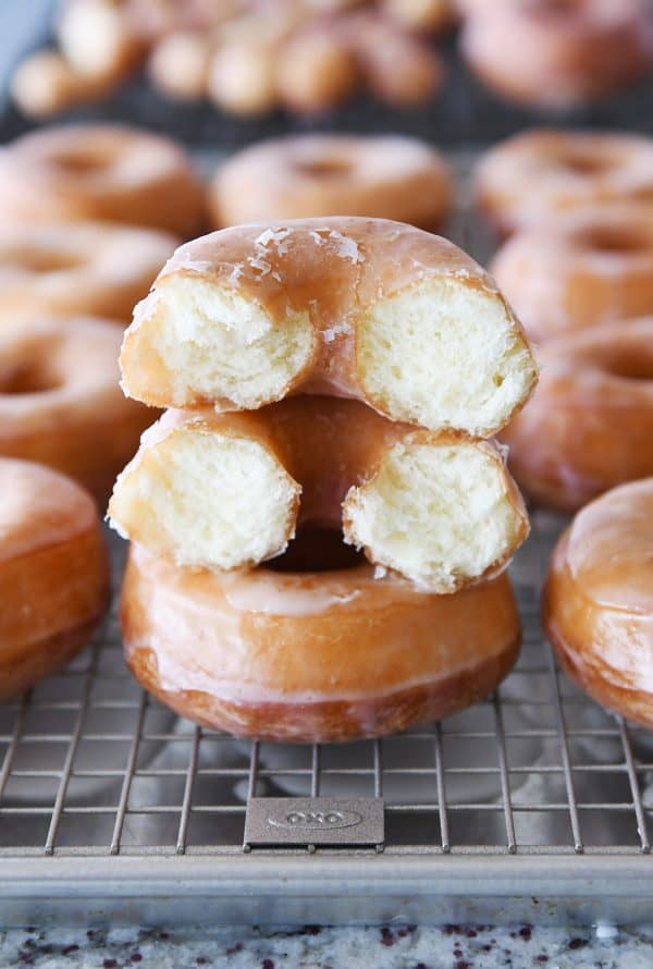 Stacked homemade glazed donuts with one broken in half.