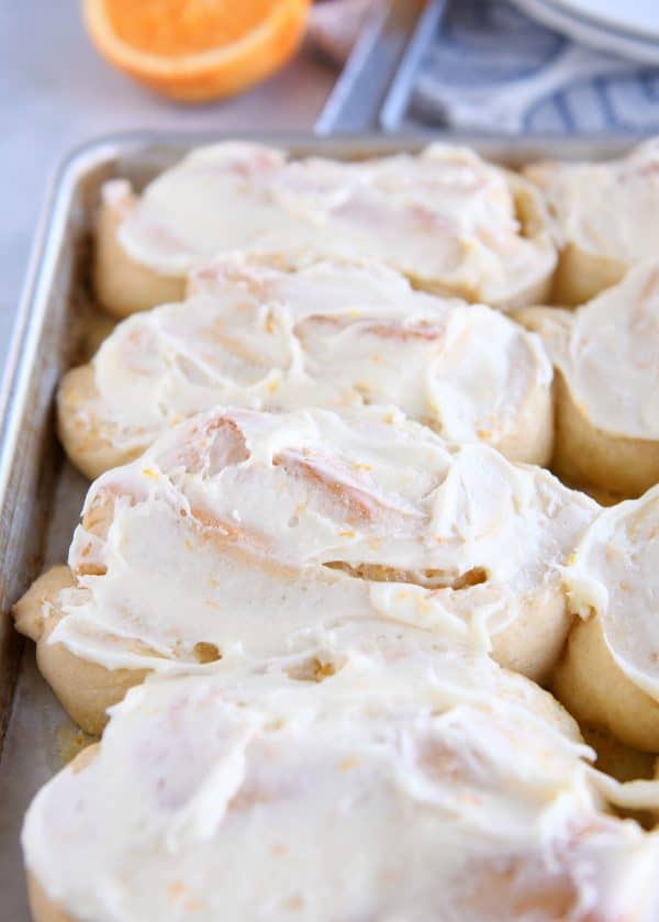 Baked homemade orange sweet rolls on sheet pan with frosting.