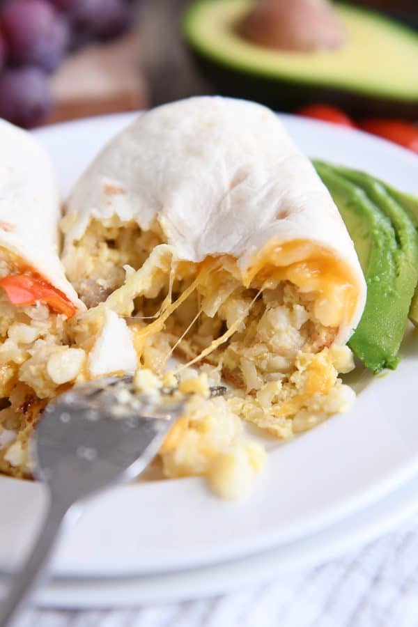 Stringy cheese pulling away on easy freezer breakfast burritos on white plate.