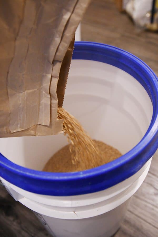 pouring wheat from brown bag into 5 gallon bucket