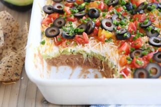 scoop taken out of 7-layer dip in white casserole dish