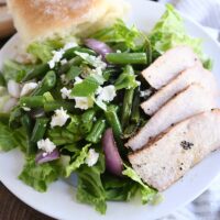 grilled pork salad with pork, red onions, green beans and roll on white plate