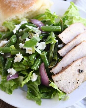 grilled pork salad with pork, red onions, green beans and roll on white plate