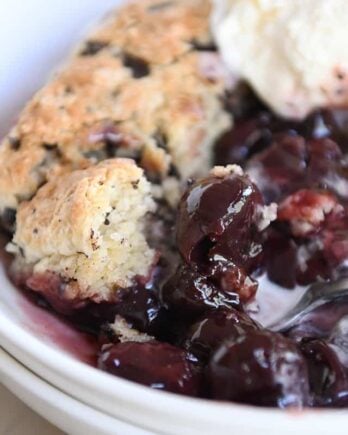 serving of cherry chocolate cobbler with chocolate chunk biscuit and vanilla ice cream in white bowl