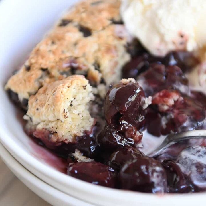 serving of cherry chocolate cobbler with chocolate chunk biscuit and vanilla ice cream in white bowl