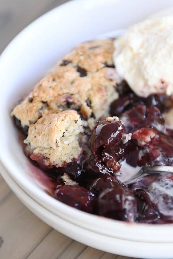 spoon digging into bowl with cherry cobbler and chocolate chunk biscuit