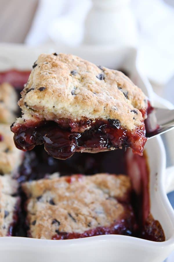 Lifting scoop of chocolate chunk cherry cobbler out of dish with spatula.