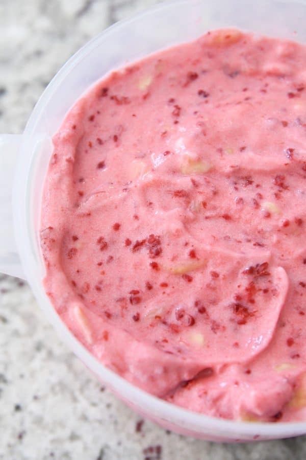 Fruity pink sorbet spread into freezer container.