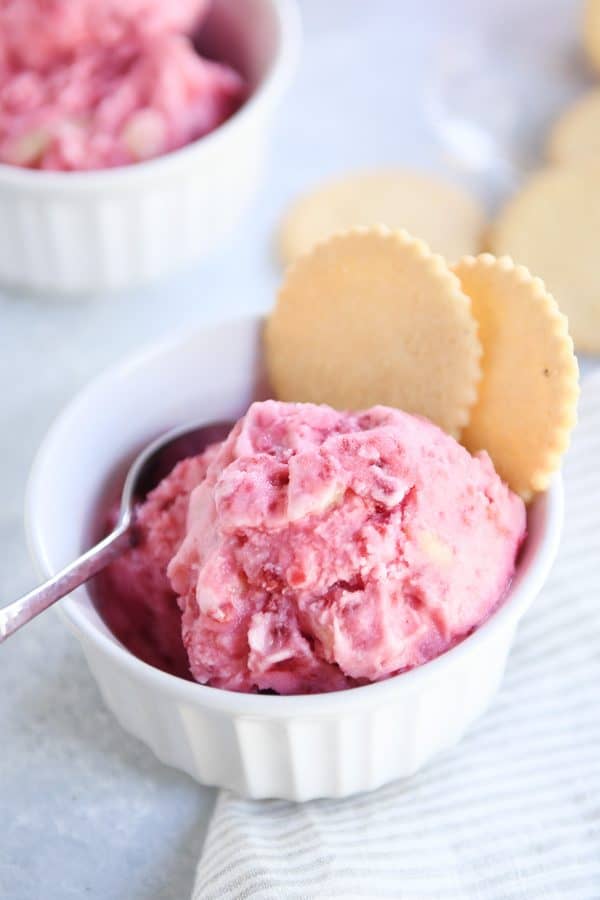 Scoop of fruity pink sorbet in white dish with two lemon cookies.