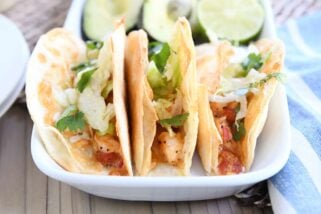 three crispy shrimp tacos in flour tortillas with lettuce on white tray